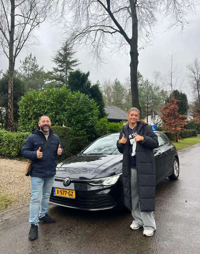 Geslaagde leerling naast de lesauto